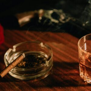 A warm, moody scene with a cigar, whiskey glass, and a red rose on a wooden table.