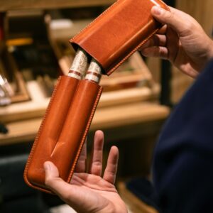 Hands holding premium cigars in a luxury leather case, showcasing elegance and style.